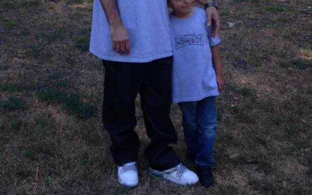Father with his arm around his young son, whose T-shirt says "Little Homeboy"