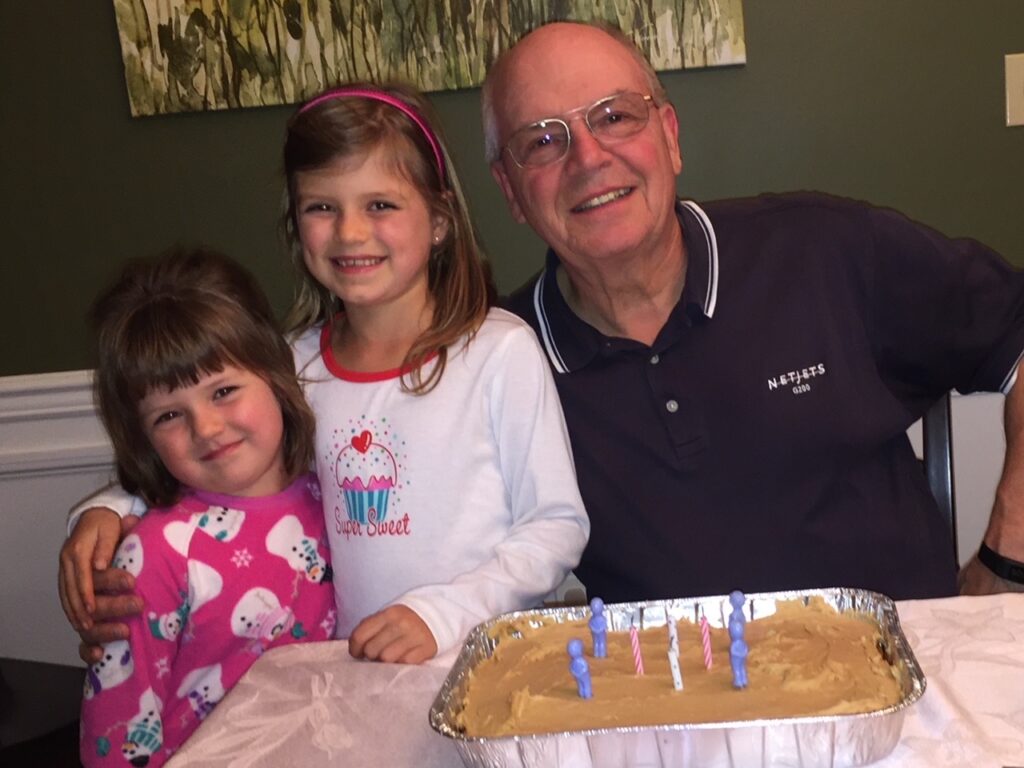 Photo of Jennifer Acker's father—a smiling, balding older white man with glasses—and her two young daughters, who both have brown hair and smiles