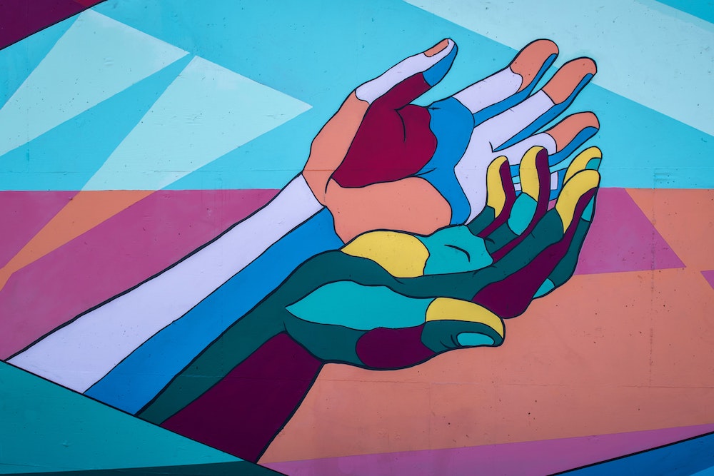 Mural depicting two outstretched hands in bright blues, purples, and greens, with yellow and peach highlights
