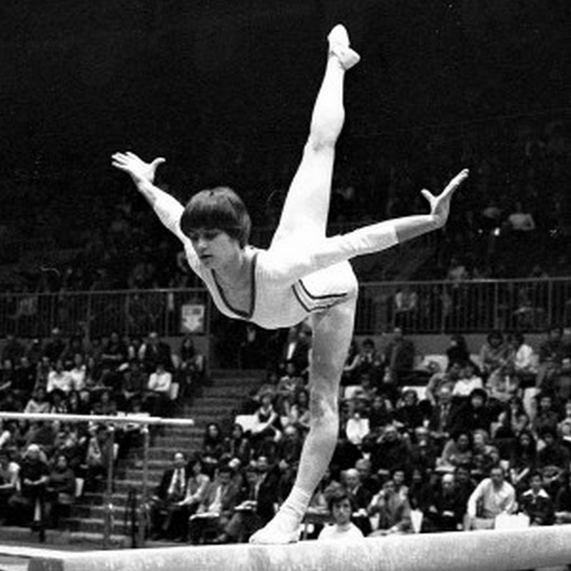 Nadia Comaneci on the balance beam with her right leg raised in a split behind her