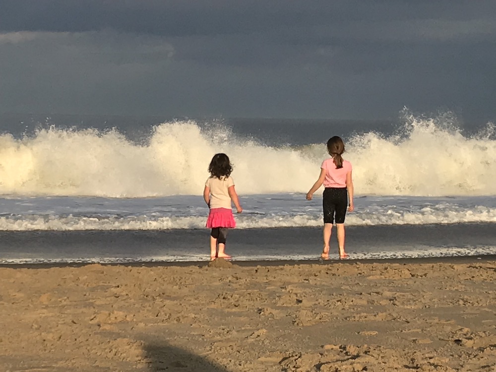 Two small children stand on the beach facing the ocean
