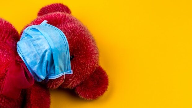 A bright pinkish-red teddy bear with a blue face mask against a yellow background
