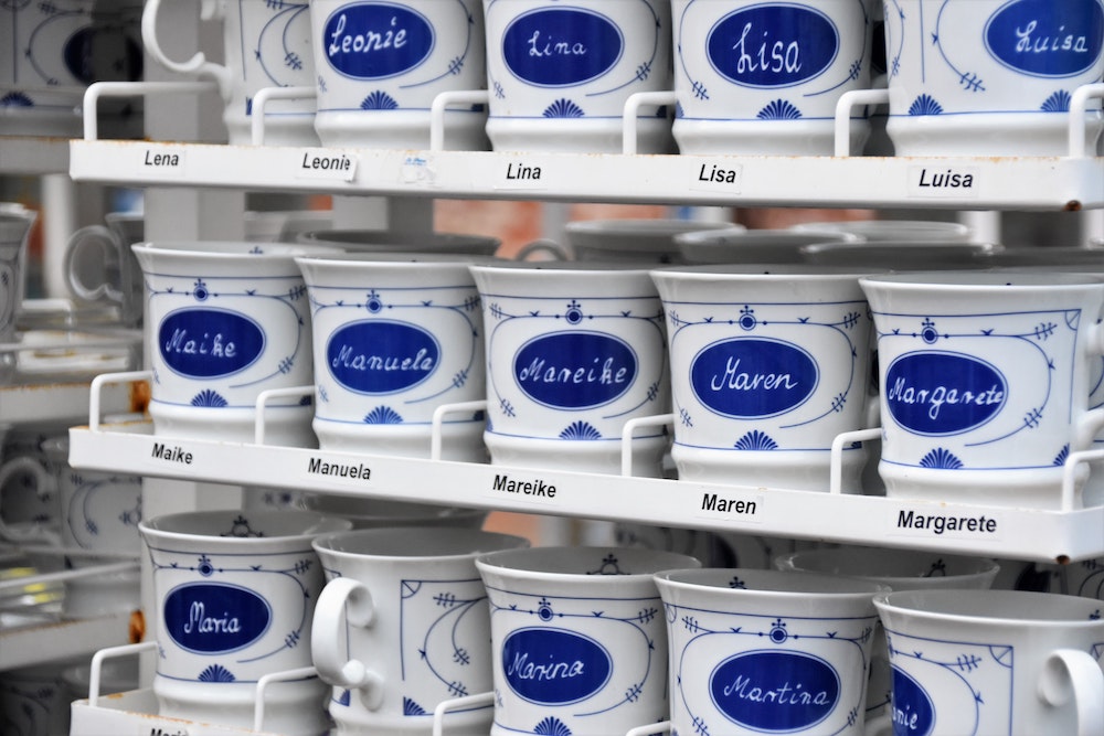 Rows of blue and white mugs on shelves in a store. Each has a different girl's name: Maike, Manuela, Mareike, etc.