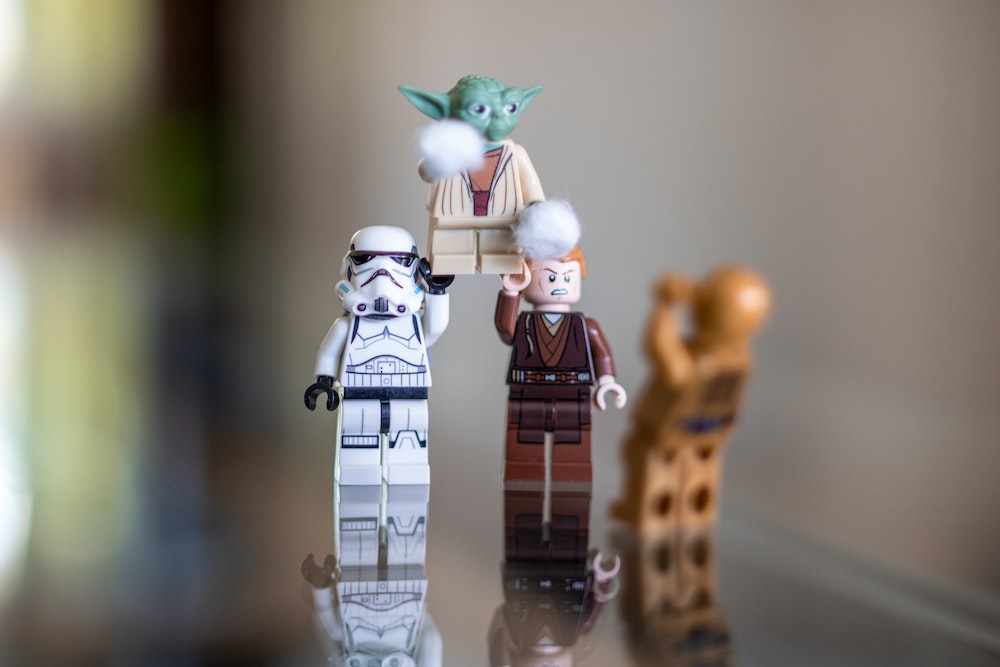 Several Star Wars LEGO figures: A Stormtrooper and Luke Skywalker carry Yoda above their heads as C3PO looks on.