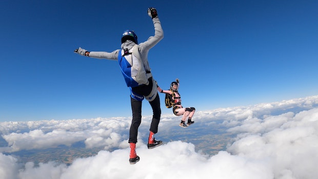 Two figures skydiving above the clouds; their parachutes are not yet visible