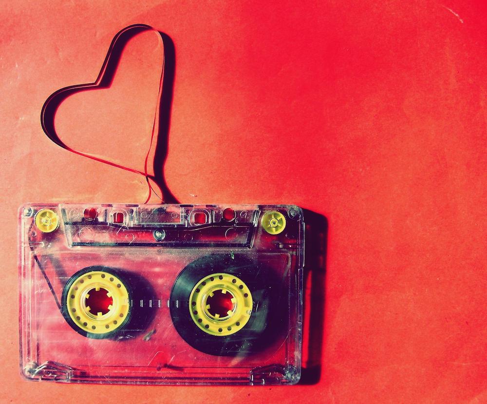 Cassette tape against a red background. Loose tape unspooling from the top forms a heart shape.