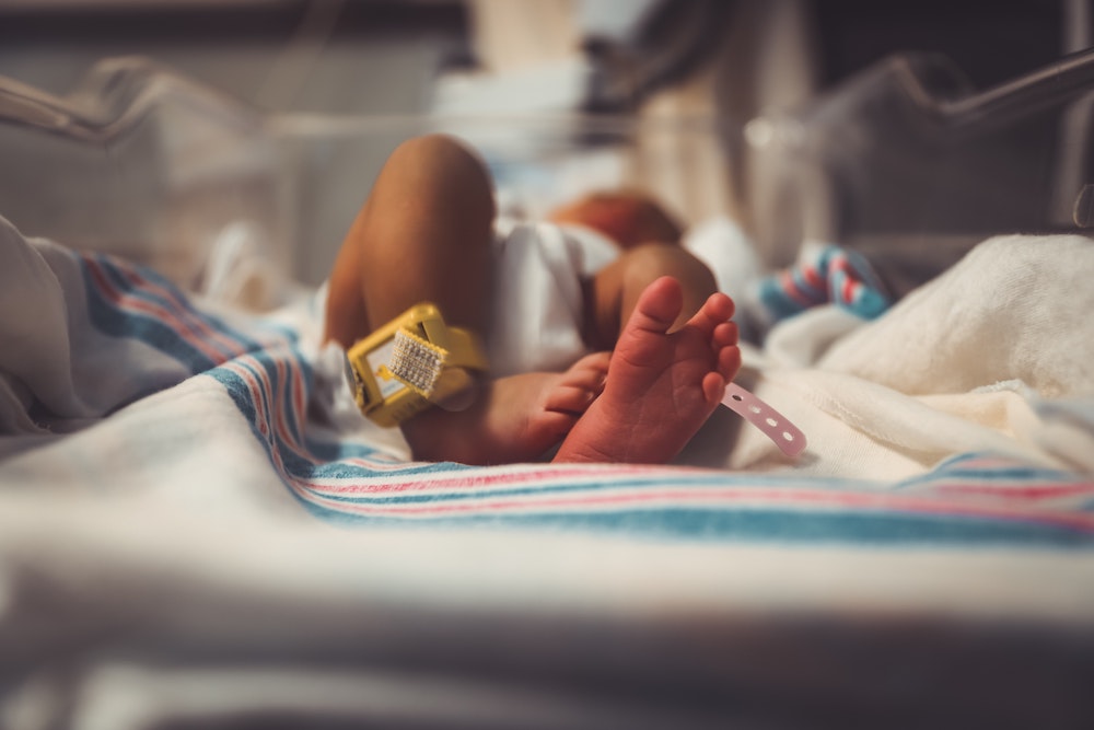 A newborn, viewed feet first, in a hospital nursery bed, with hospital bracelets on their ankles