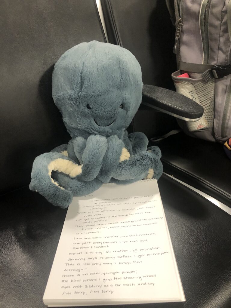 Stuffed blue octopus sits on top a notebook on a black vinyl chair