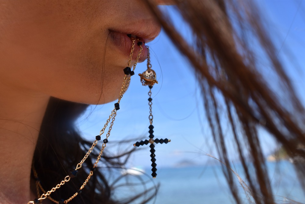 Close-up of the bottom half of a woman's face; she is holding a rosary between her lips