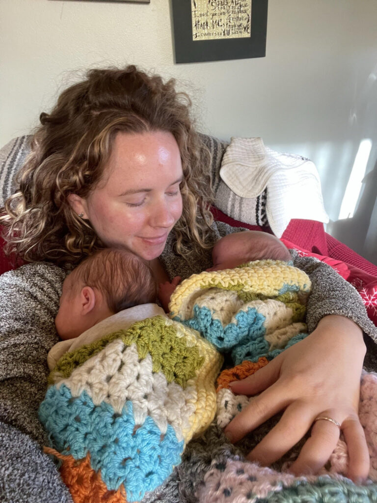 White woman with wavy hair holds twin babies in a crocheted blanket