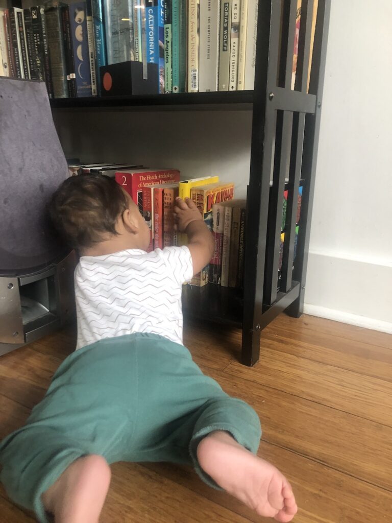 A baby reaches to grab a book from a bookshelf