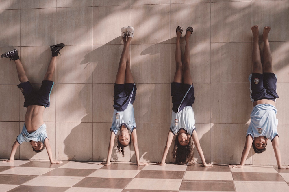 Four children wearing matching blue gym uniforms stand on their hands against a wall