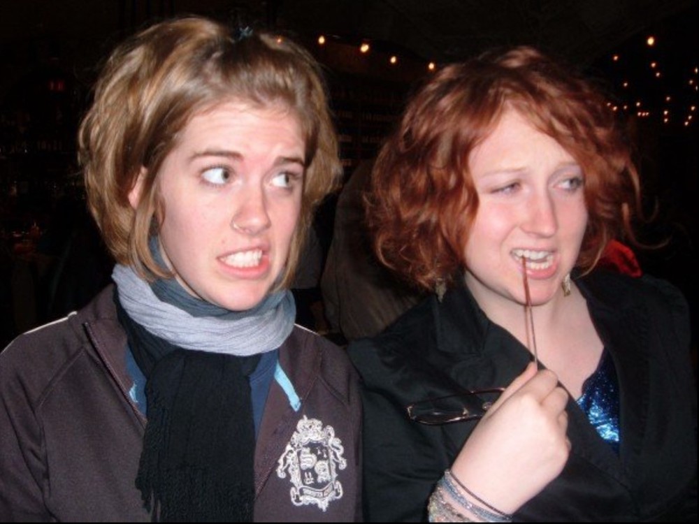 Two young women (one blonde, one with red hair) make silly, skeptical faces as they side-eye something to the right of the photo
