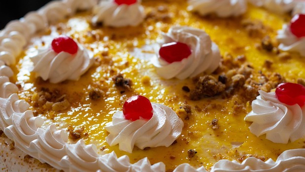 Top of a cake with dollops of whip cream and bright red cherries