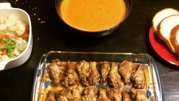 Casserole dish containing chicken thighs, with soup and bread nearby