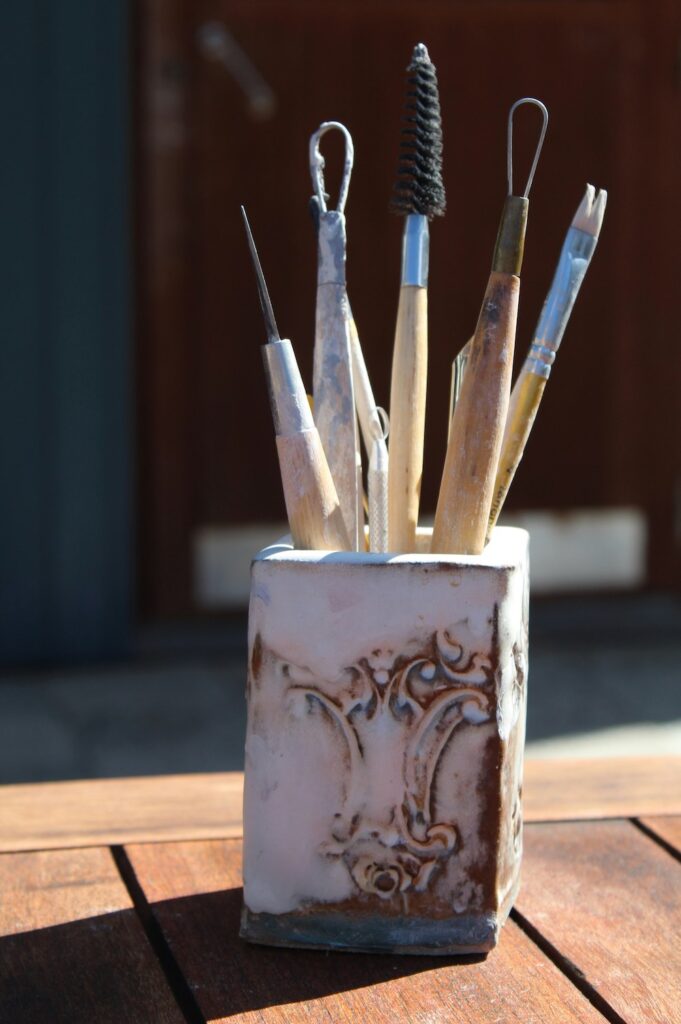 Clay container holding wooden and metal tools used to add detail on pottery