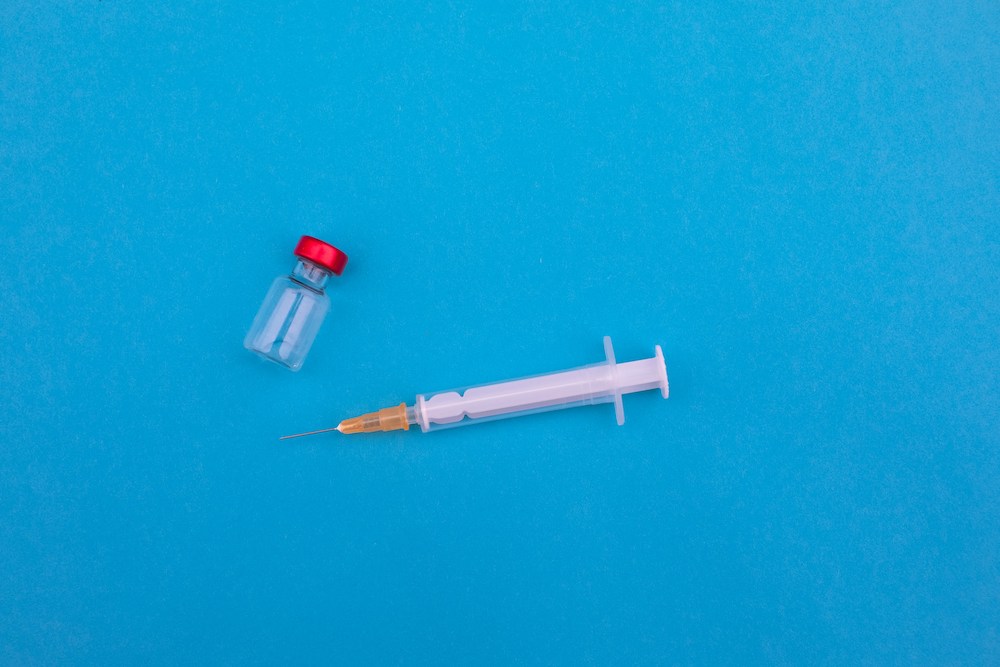 A syringe and a glass medicine vial on a blue backround
