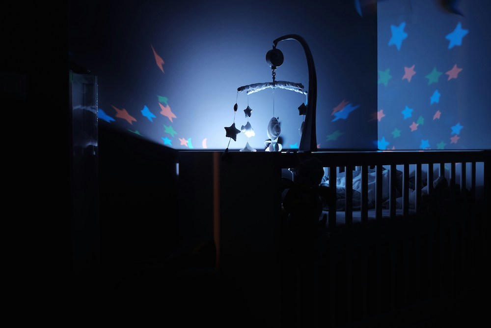 A glowing mobile casts illuminated stars on the walls of a dark nursery