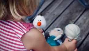 Blonde-haired child playing with dolls from Frozen