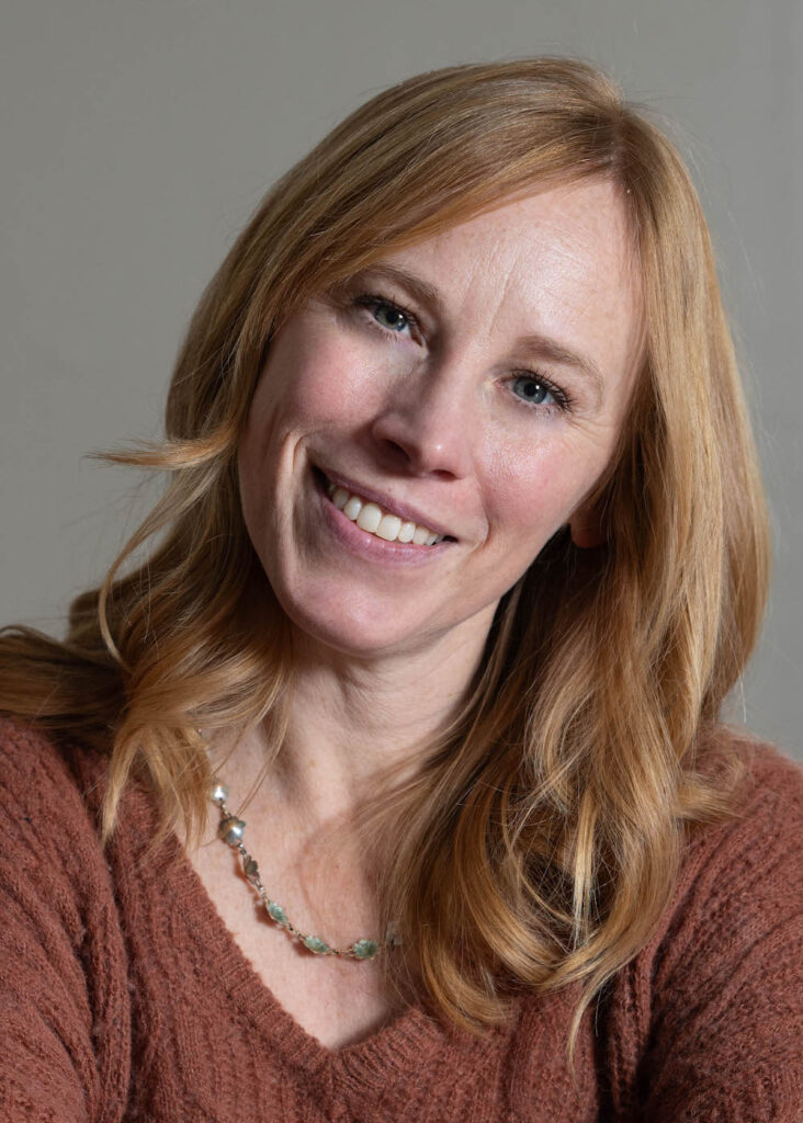 Tiffany Graham Charkosky smiles and wears a brown sweater and beaded necklace