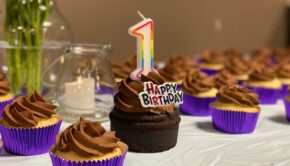 Chocolate cupcakes on a table. The middle one has a "1" candle on it and says "Happy Birthday."