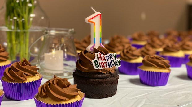 Chocolate cupcakes on a table. The middle one has a "1" candle on it and says "Happy Birthday."