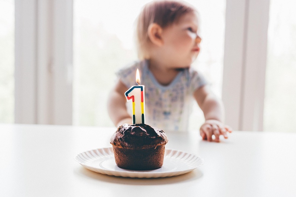 Close-up of a cupcake with a "1" candle, and a toddler behind it