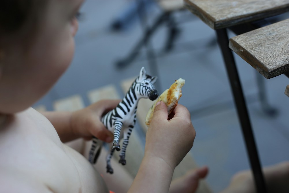 A toddler pretending to give food to a plastic zebra