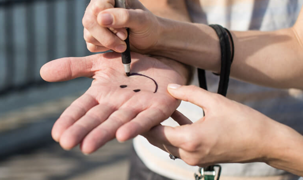 Close-up of a person drawing a happy face on another person's palm