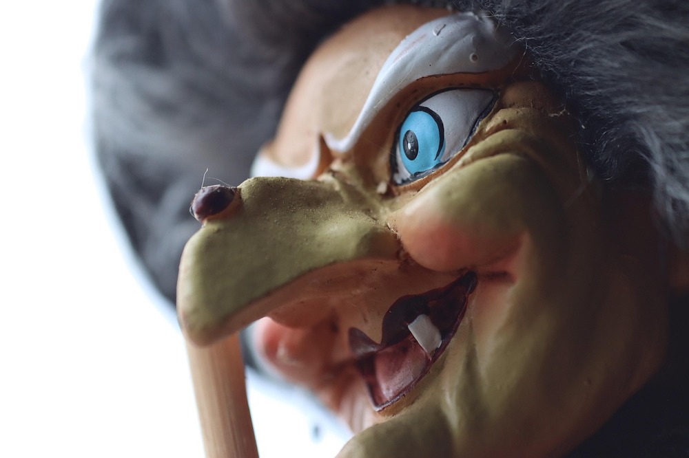 Face of a witch figurine with green skin, a big nose, and missing teeth