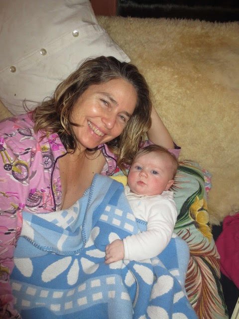 Aerial view of a woman with light tan skin and a partially open pink shirt next to a baby wrapped in a blue and white blanket