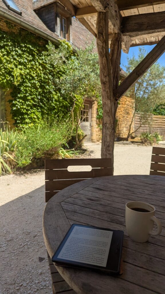 A wooden outdoor table with a cup of coffee and a tablet on it