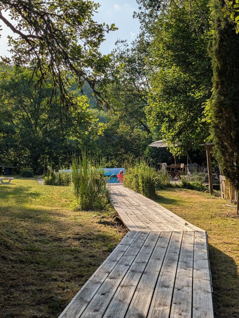Wooden walkway leading to a swimming pool in a green yard