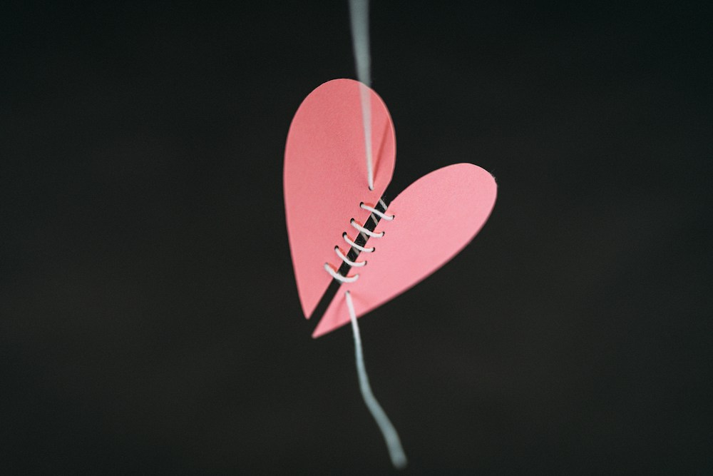 Two halves of a pink paper heart stitched together