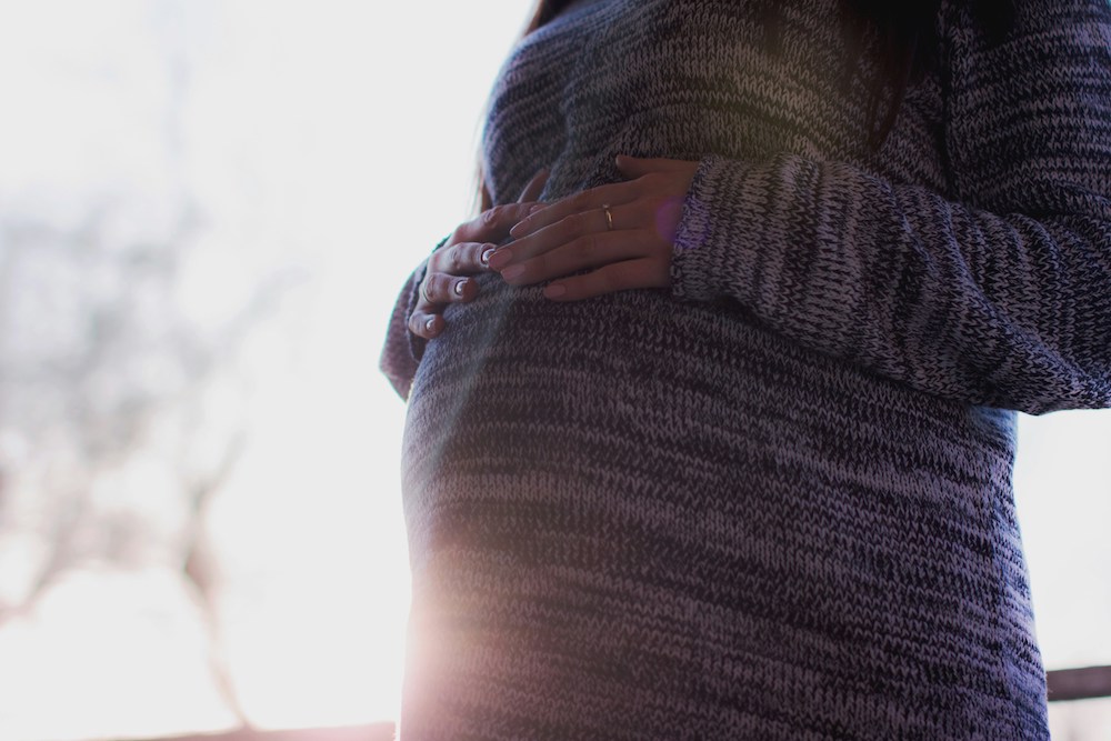 Woman in a long sweater puts her hands over her pregnant belly