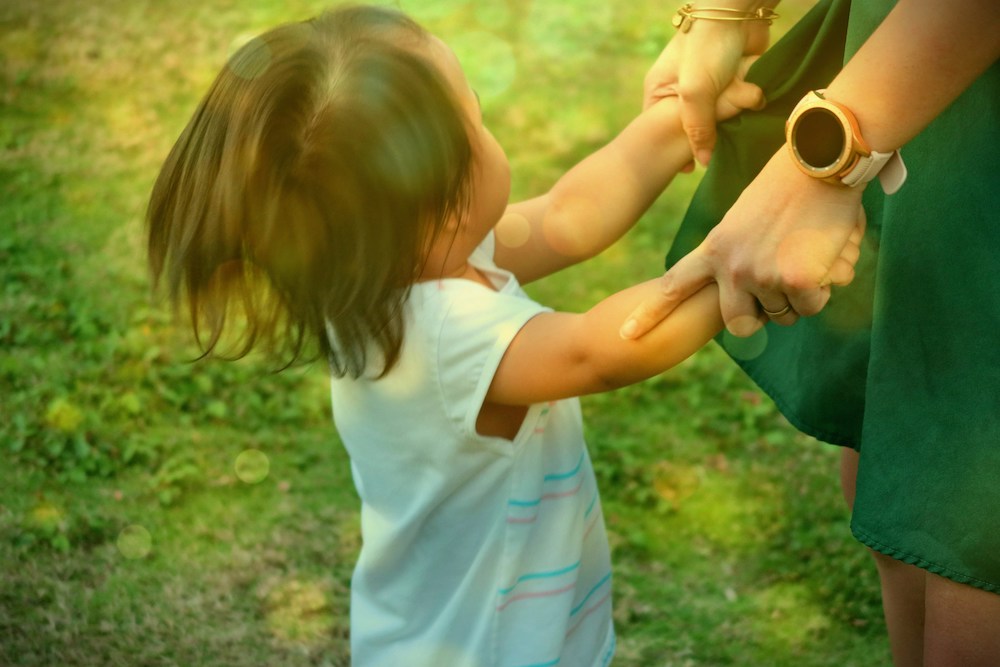 A mother's hands grip the forearms of a toddler in motion