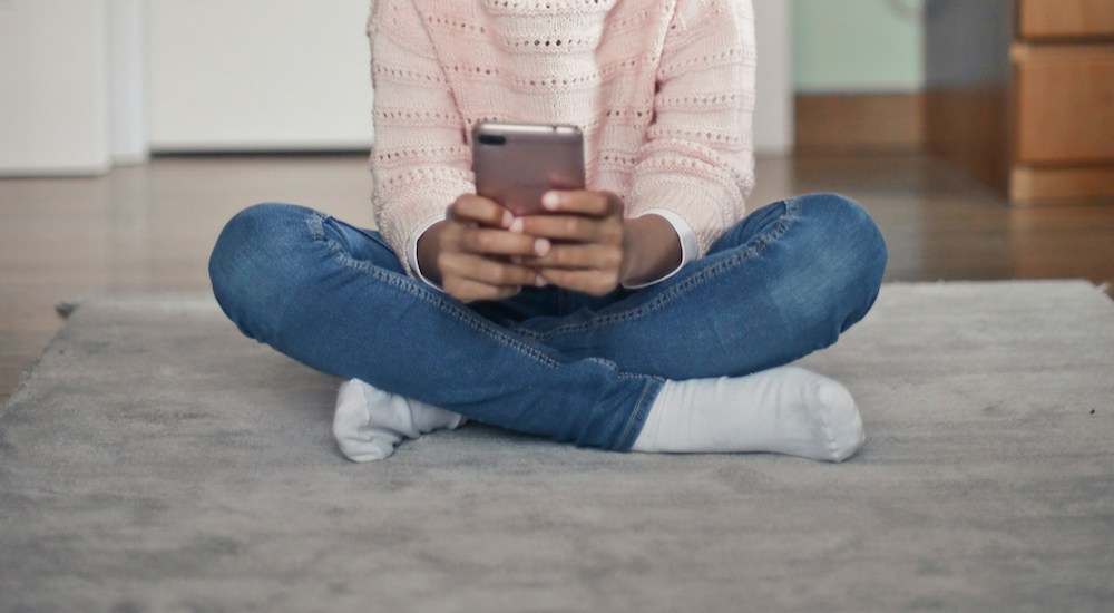 Girl in pink sweater and jeans with medium brown skin, looking at a phone