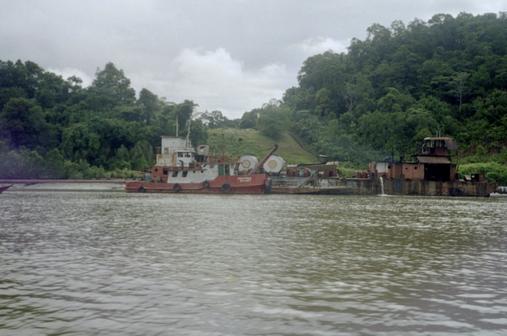 Rusty oil tanker on a river with lush green trees on the bank