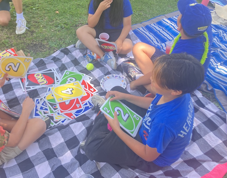 Fifth graders play Uno on a checked picnic blanket