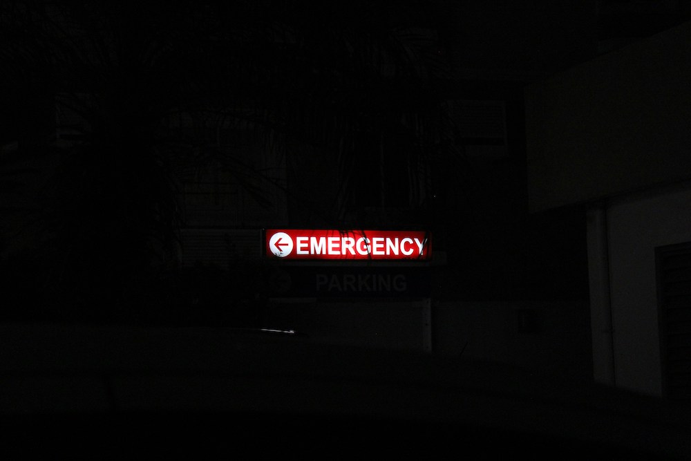 Against a dark background, a backlit sign says "EMERGENCY" with an arrow pointing to the left