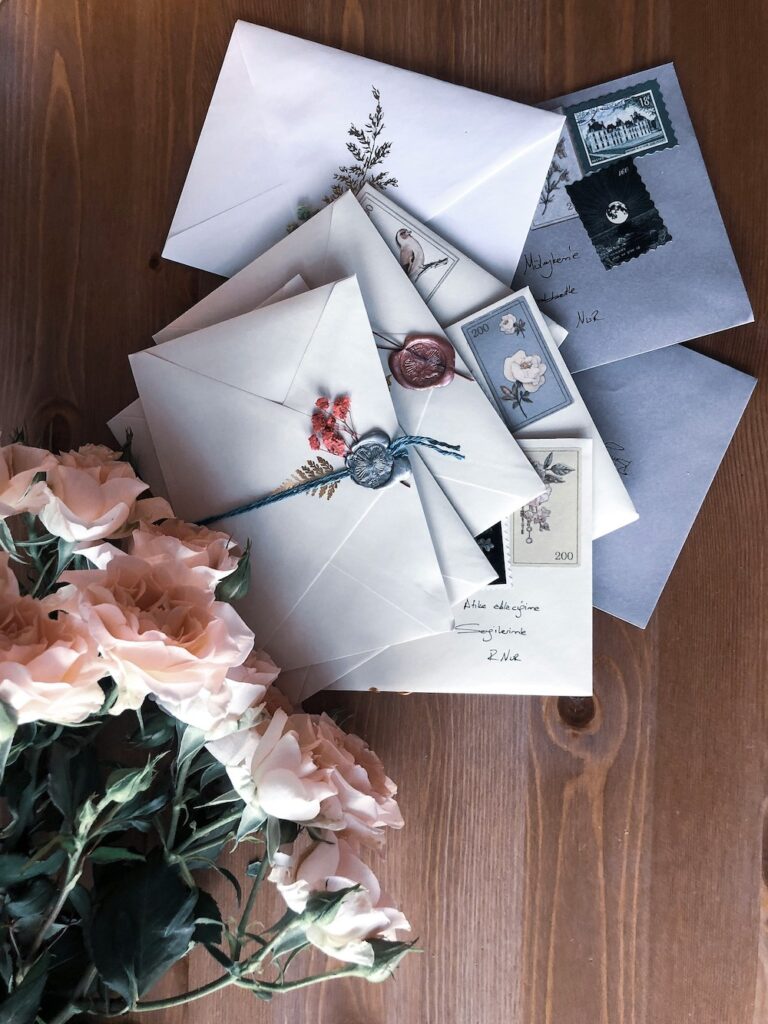 Pile of letters, stamped and sealed with was, next to a bouquet of pink flowers