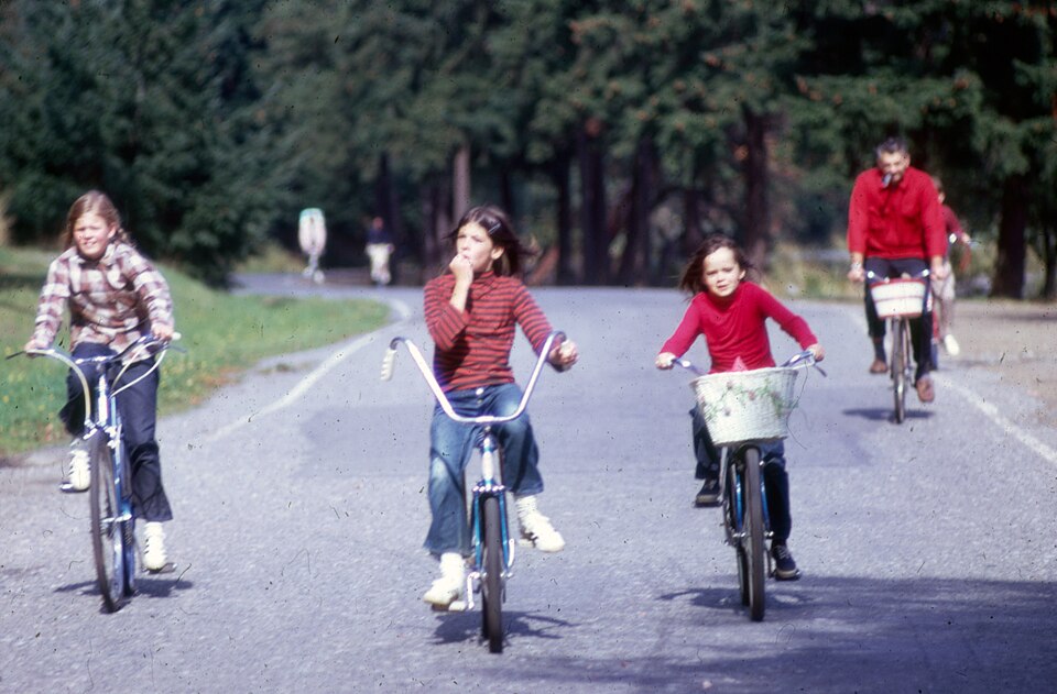 Children in 1980s clothing riding bikes down the middle of the street
