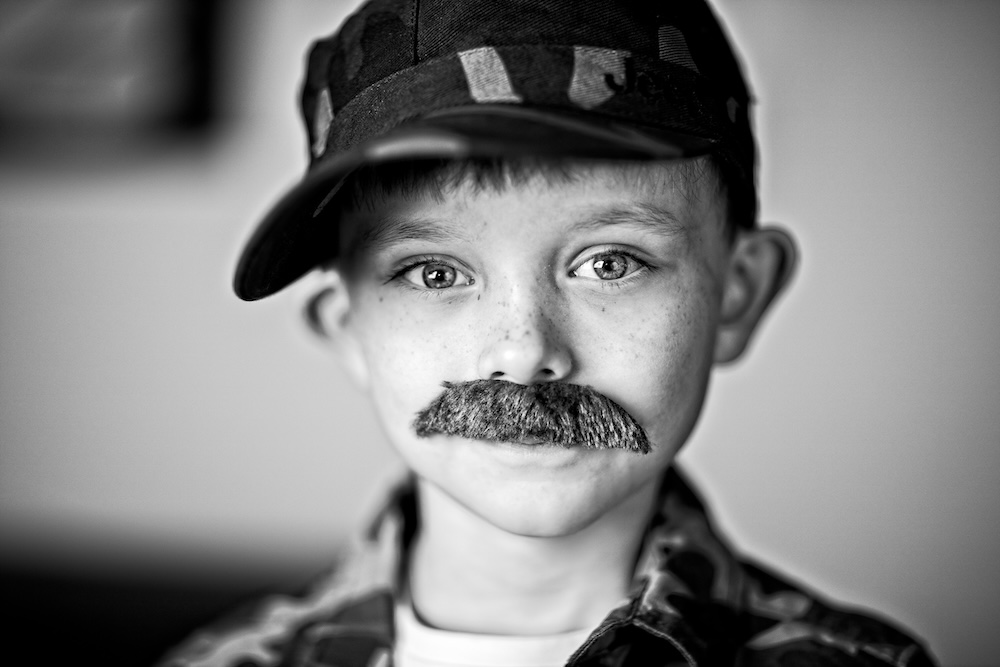 Black and white photo of a young boy wearing a hat and fake mustache