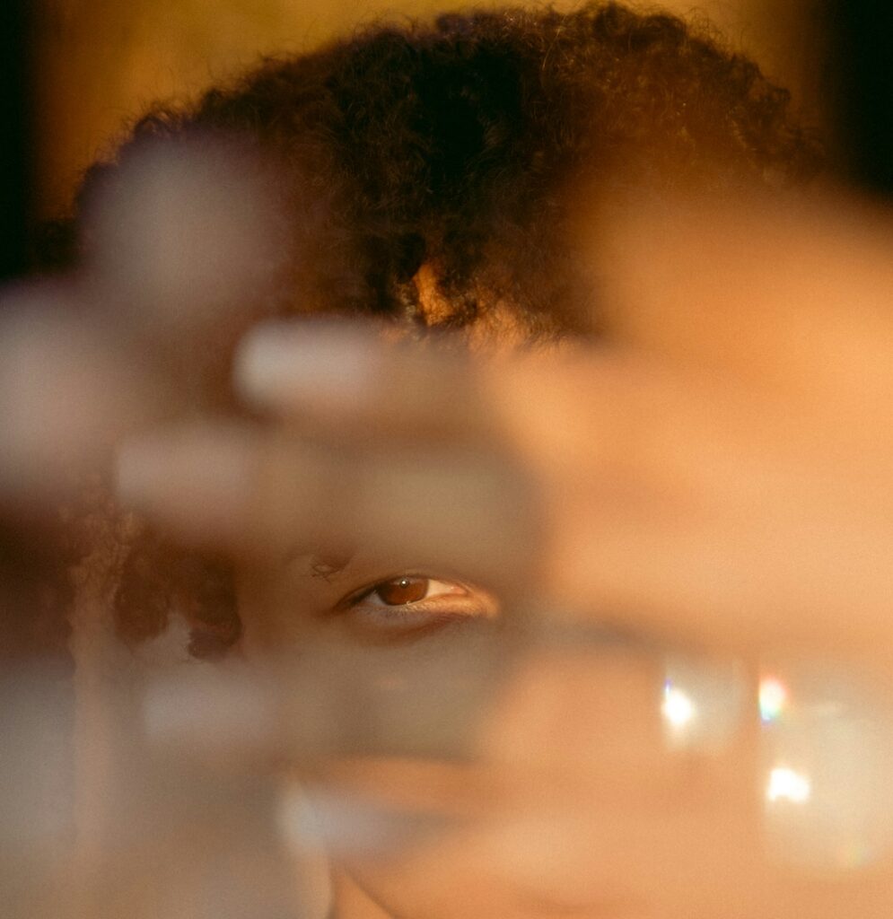 Blurry photo of a young woman or girl with light brown skin and curly brown hair peeking through her fingers